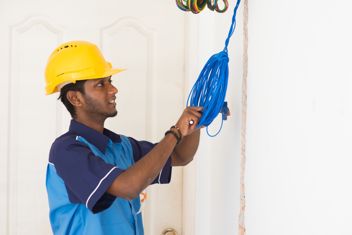man wearing a yellow hard hat adjusting wires in a home
