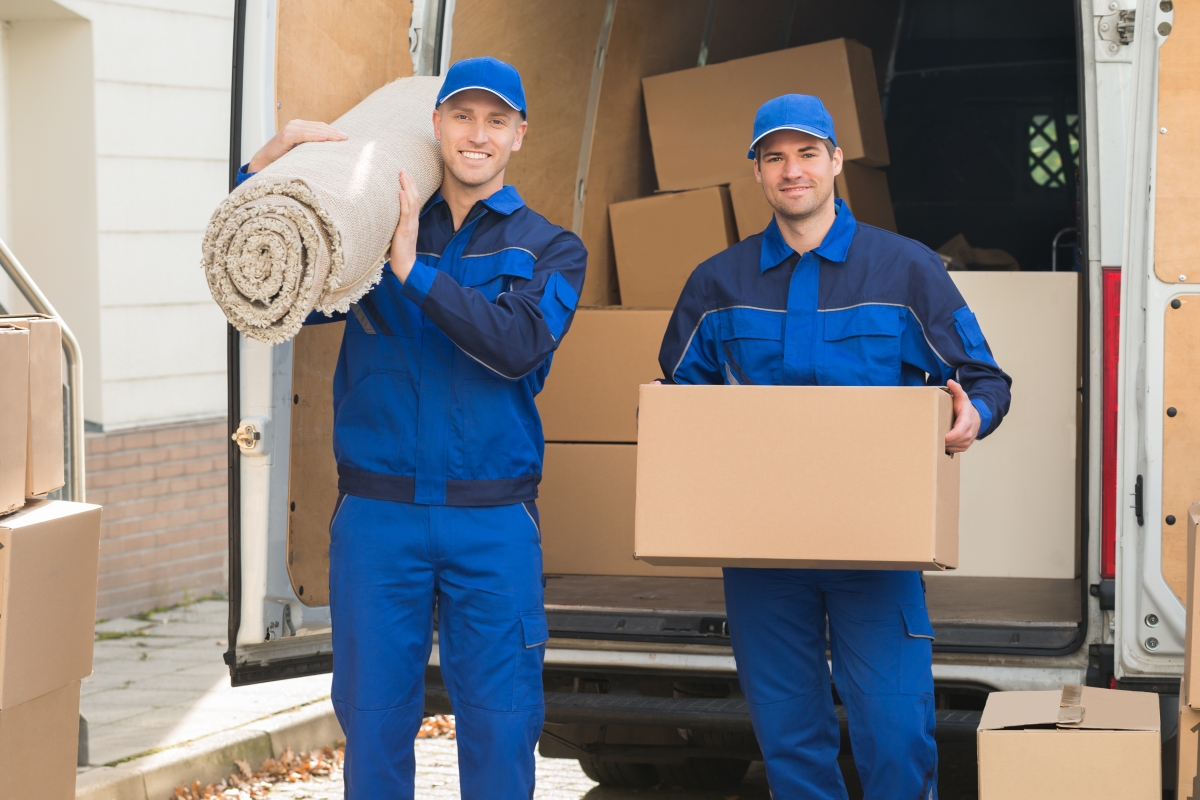 two men in matching blue hats and uniforms unloading boxes and other items from a van