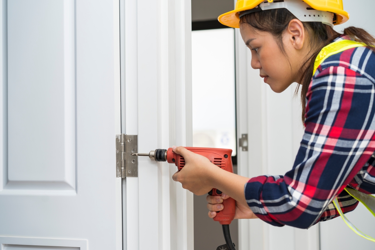 woman wearing hard hat using a power drill on a door hinge