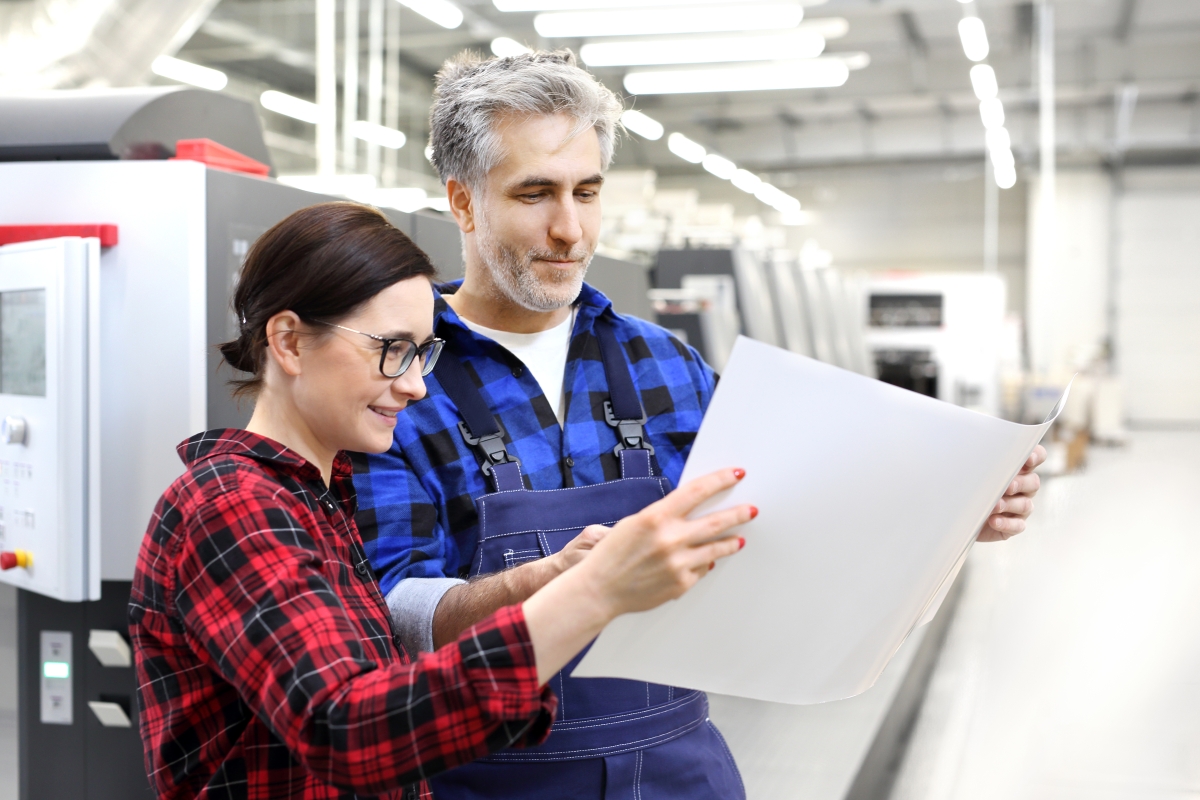 man and woman in plaid shirts reviewing a large document in an industrial setting