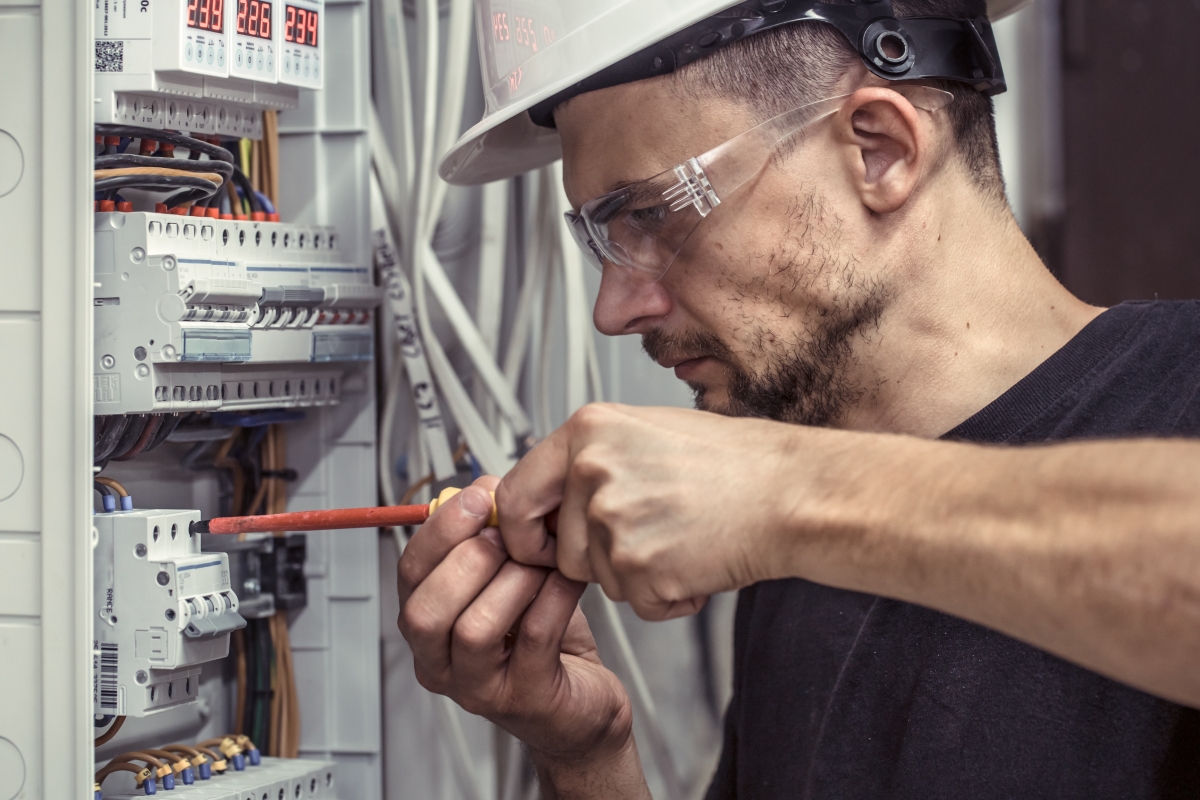 man wearing hard hat and safety glasses using a tool to work on an electrical panel