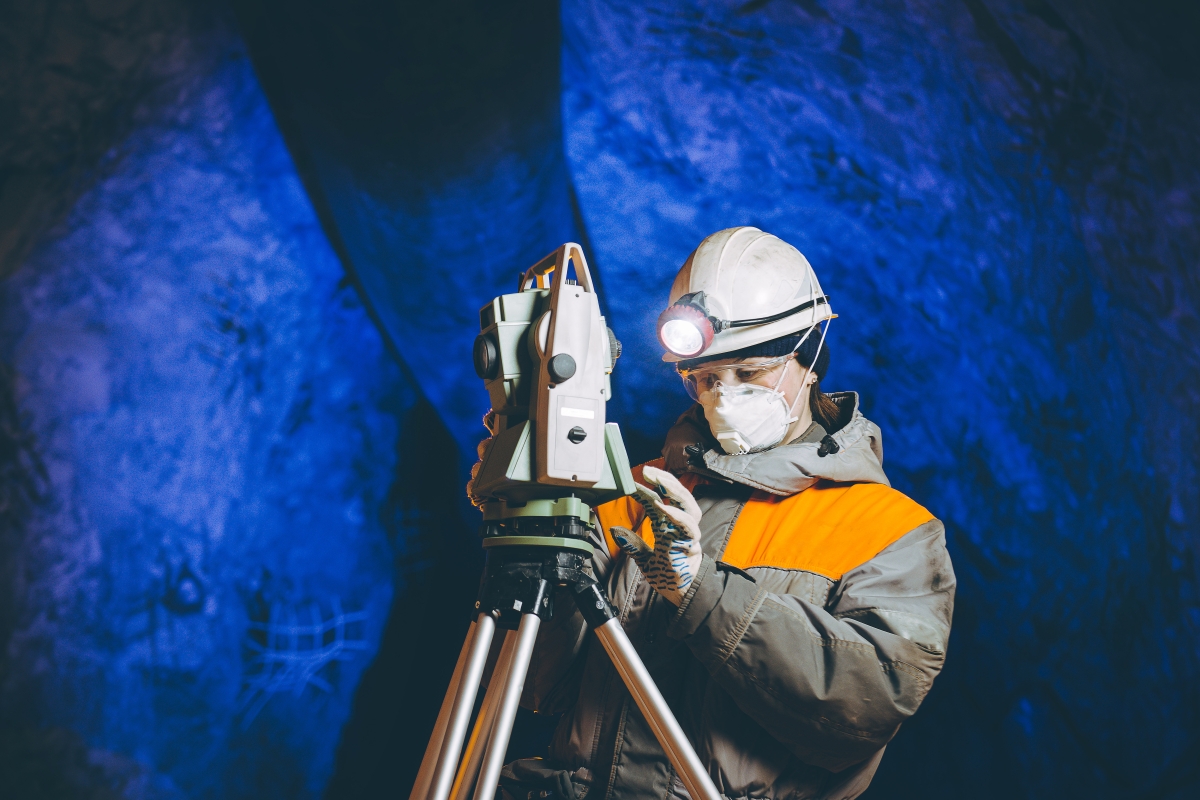 person wearing a safety vest, hard hat with a head lamp attached, a face mask and gloves while using equipment for underground analysis