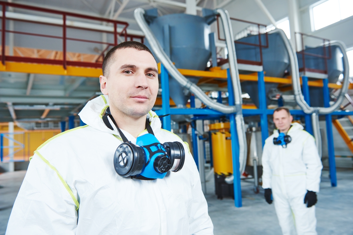 two people, wearing protective overalls and masks, standing in an industrial setting