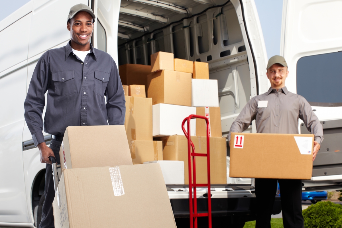 two diverse male postal workers smiling while unloading boxes from a delivery van
