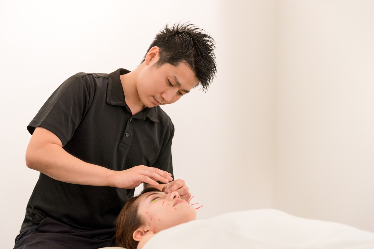 person standing and putting acupuncture needles into their patient's face