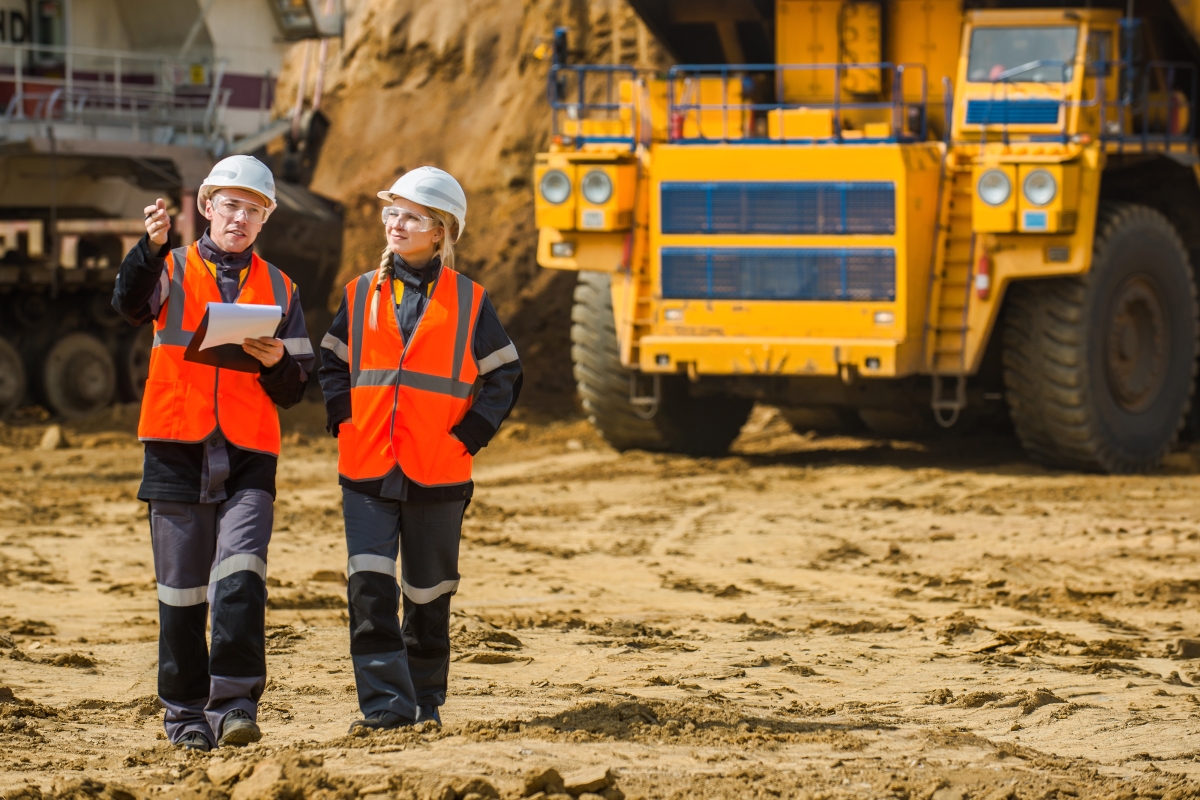 two people in hard hats, safety vests and safety glasses looking around a construction site