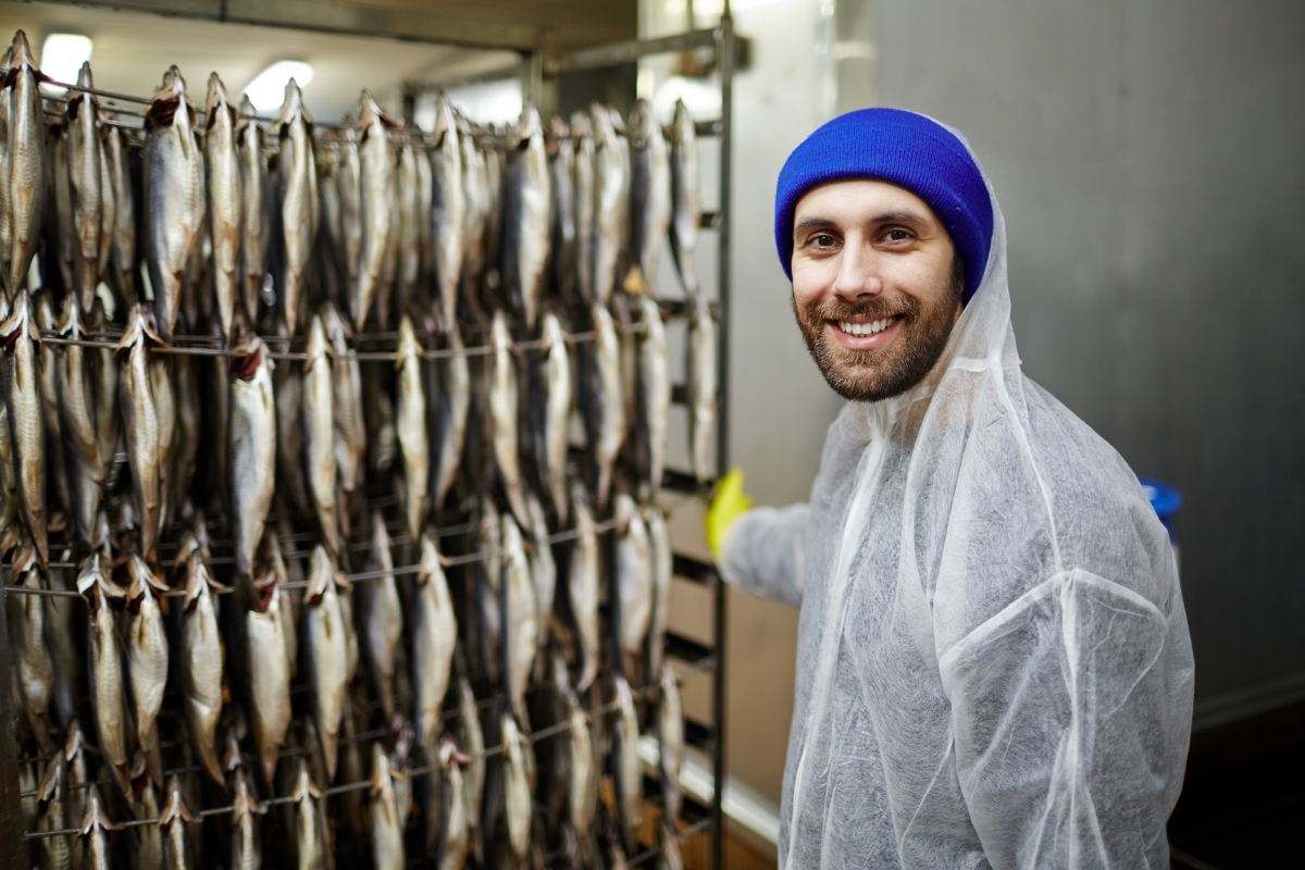 person, wearing a toque and a plastic raincoat, standing in front of a rack of hanging fish