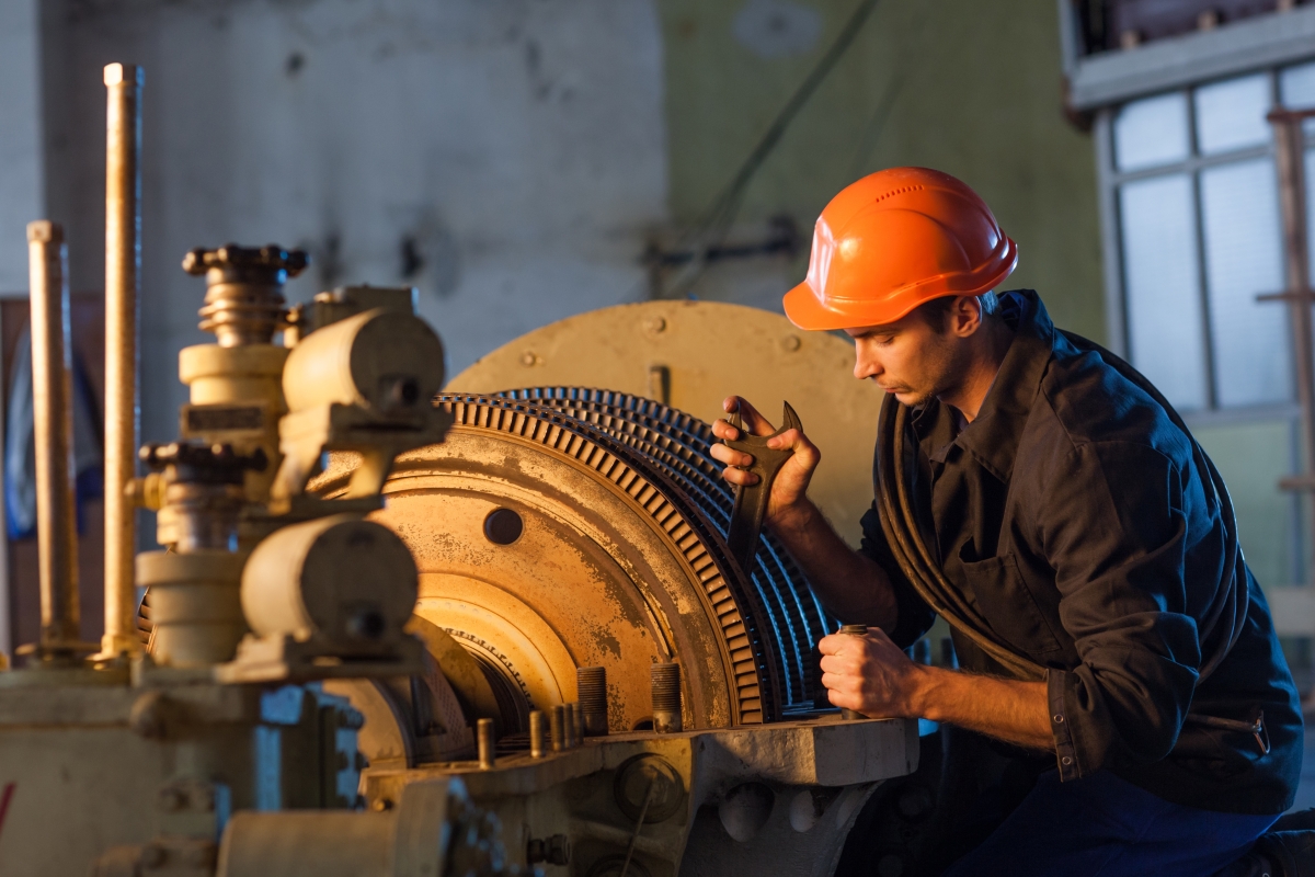 man in orange hard hat using tools to work on large machinery in industrial setting