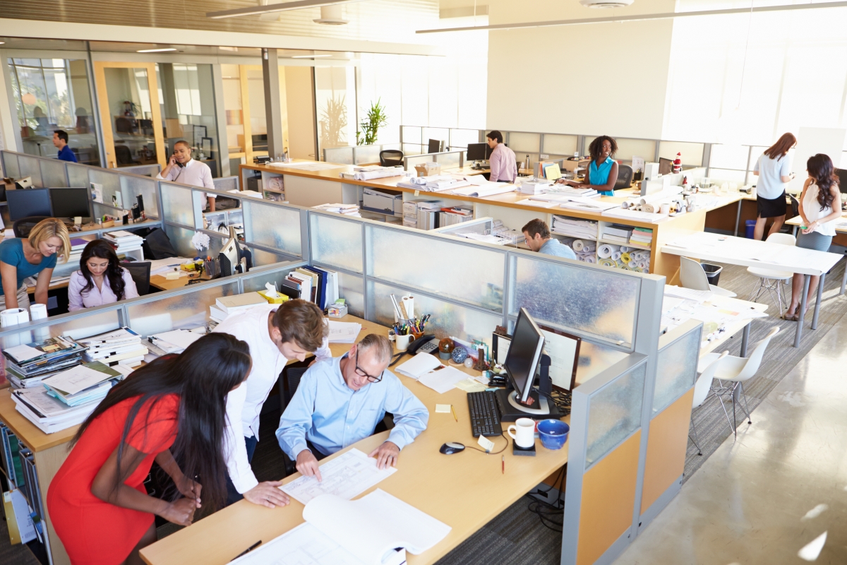 overhead view of many diverse people collaborating and working individually in office cubicles and at tables or desks with computers and documents